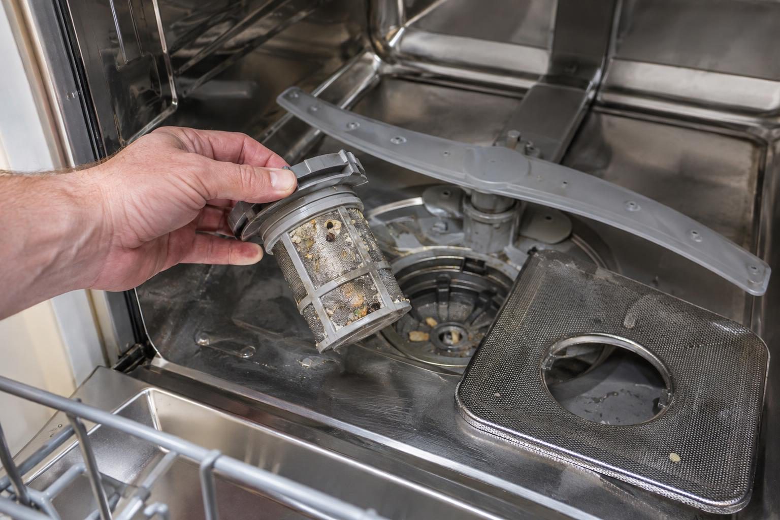 Close-up of a Bosch dishwasher drain filter being removed by hand, showing collected debris on the filter screen.